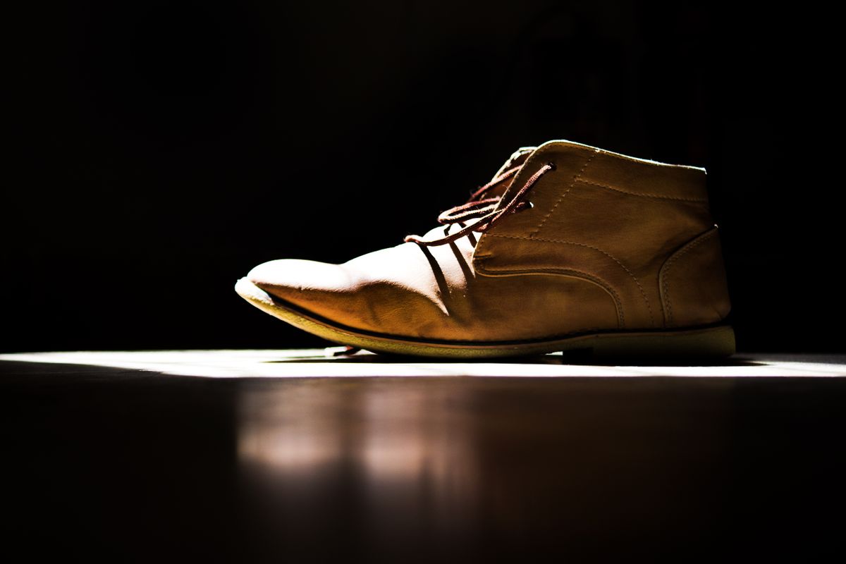 A brown leather chukka boot lit against a dark background.