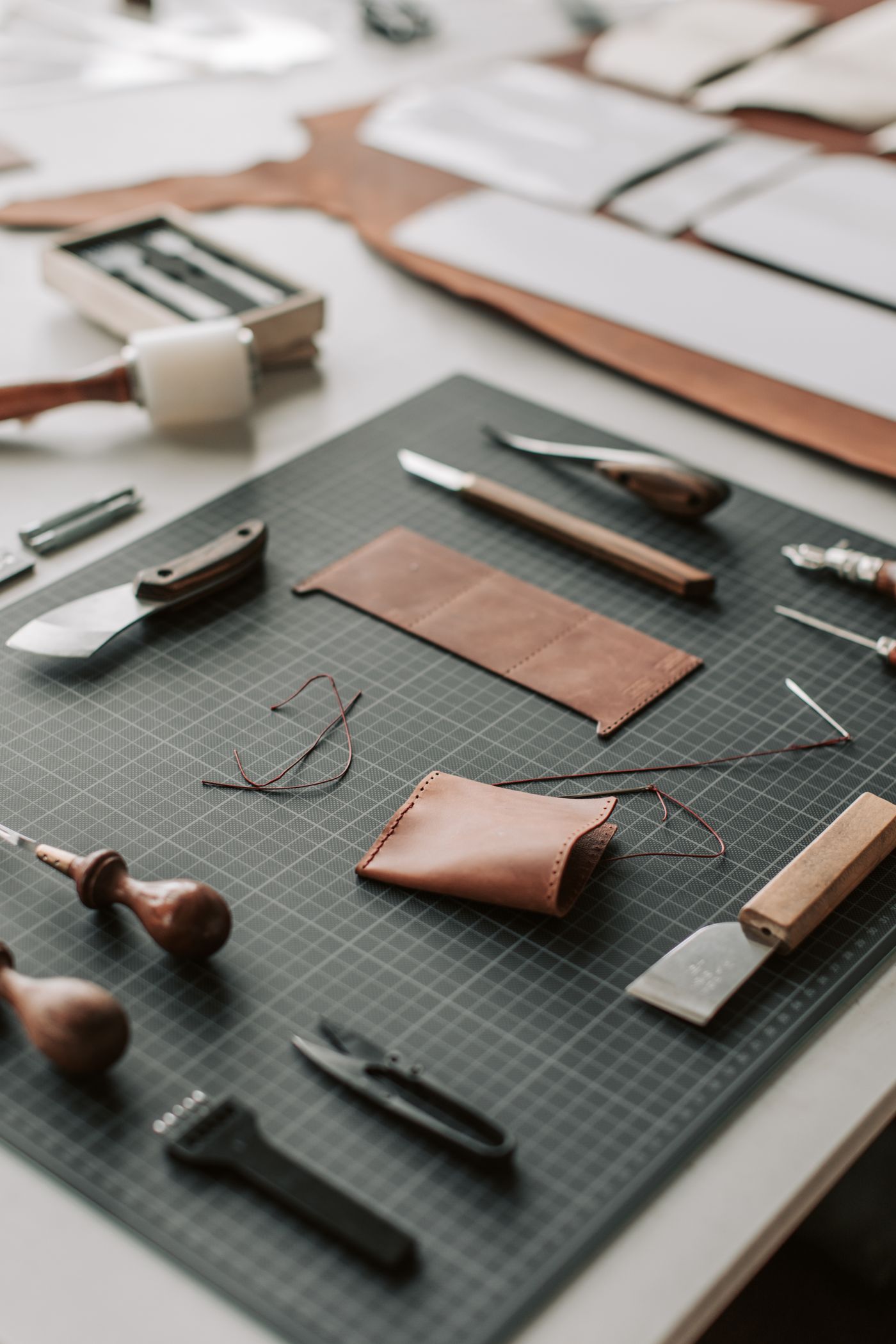 Leather working tools, thread and cut pieces laid out on a cutting mat.