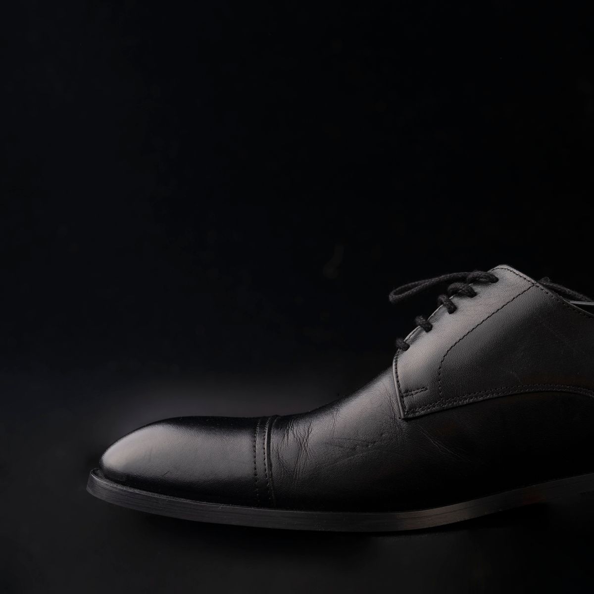 A black leather Oxford shoe on a dark background.